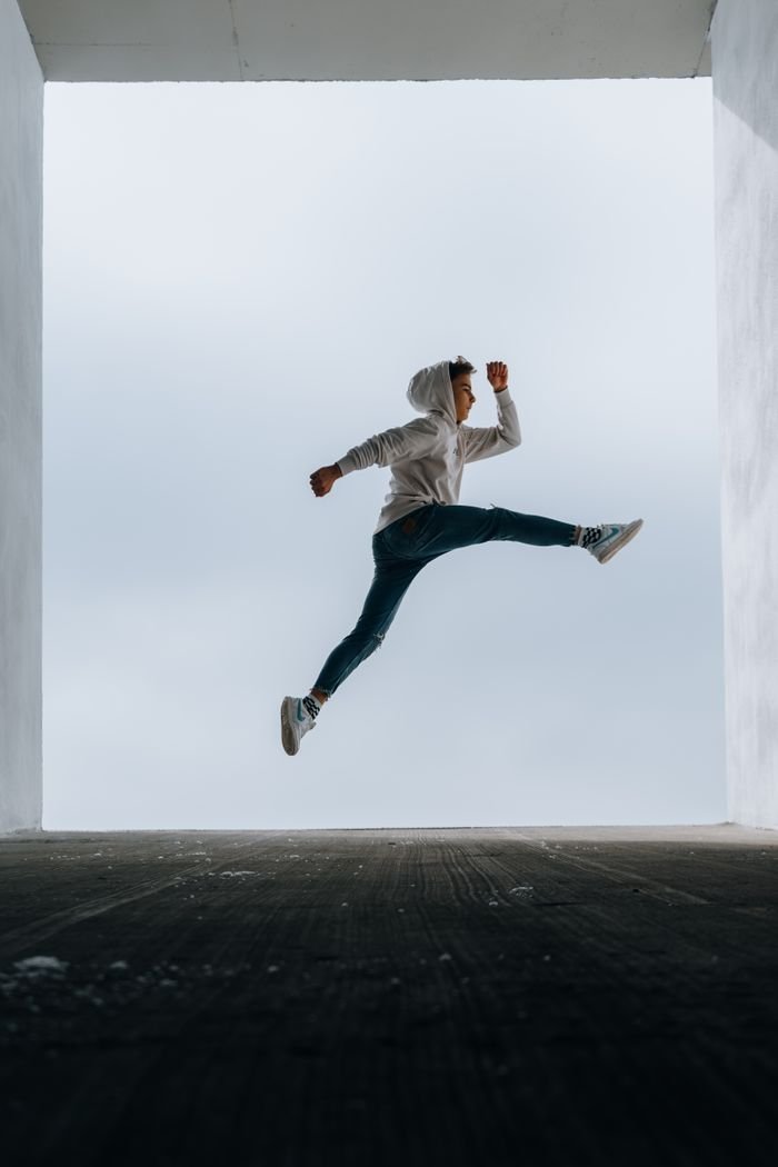 A boy in a hoodie performing a high vertical jump outdoors, showcasing athleticism and energy.